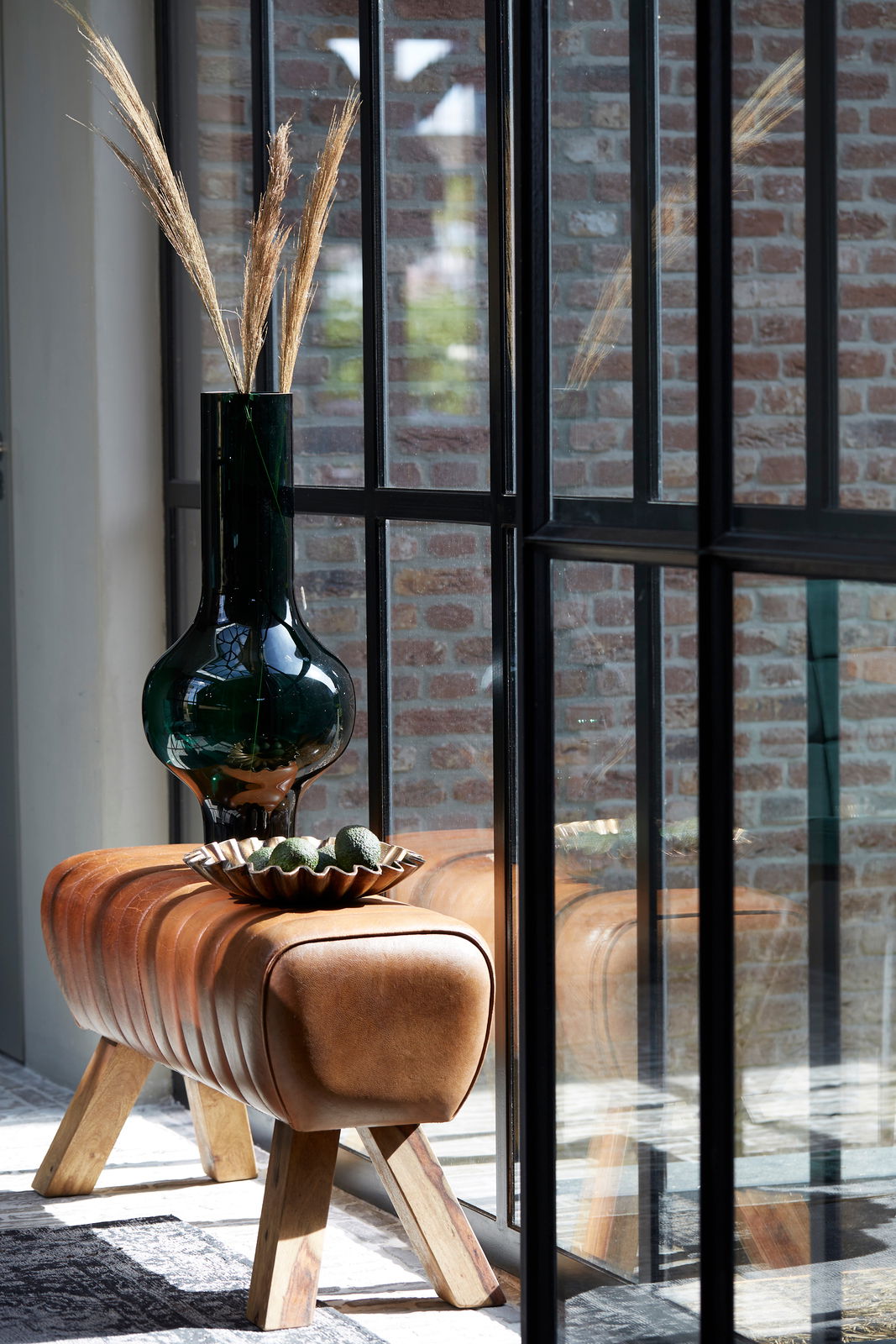 Bank aus braunem Leder mit Holzbeinen, dekoriert mit einer grünen Vase und einer Schale, seitliche Perspektive.