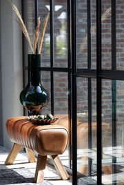 Bank aus braunem Leder mit Holzbeinen, dekoriert mit einer grünen Vase und einer Schale, seitliche Perspektive.