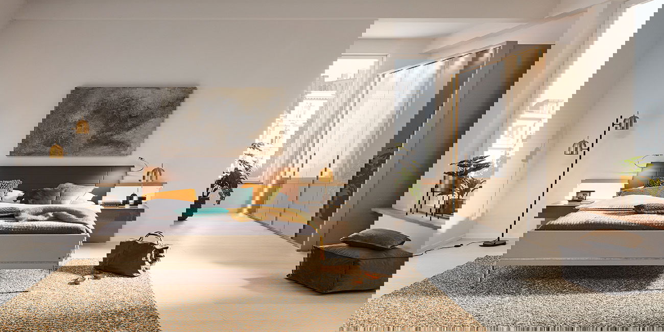 Das Bild zeigt ein modernes Schlafzimmer. In der Mitte steht ein großes Bett mit einer gemütlichen Decke und vielen Kissen in verschiedenen Farben. Links und rechts neben dem Bett sind kleine Nachttische mit Lampen. Im Hintergrund steht ein großer Kleider