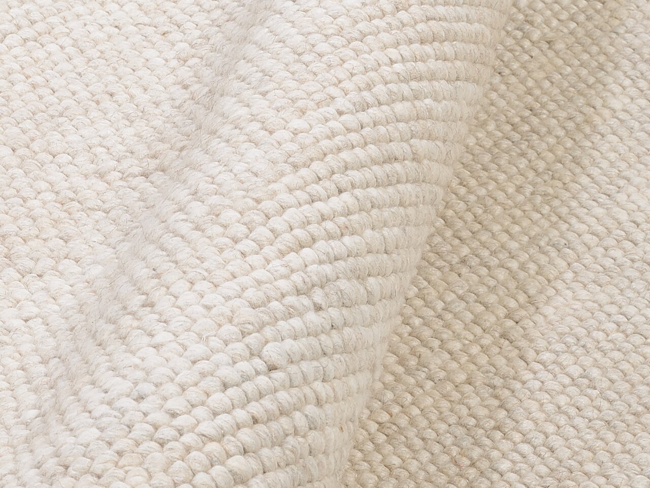 Nahaufnahme eines handgewebten Teppichs in cremeweißer Farbe, die Textur und Webart sind deutlich sichtbar, Perspektive von oben.