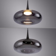 Moderne Pendelleuchte mit rauchgrauem, glänzendem Glas-Schirm in flacher, runder Form und schwarzem Kabel, warm leuchtend; Ansicht leicht von unten (Untersicht)