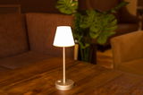 Elegante Akku-Tischleuchte LOLA slim auf einem Holztisch, seitliche Perspektive, mit warmem Lichtschein in gemütlicher Umgebung.