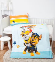 Renforcé-Bettwäsche mit buntem Paw Patrol-Motiv, bestehend aus einem Kissenbezug mit Streifenmuster und einer Bettdecke mit fröhlichen Hundemotiven, auf einem Kinderbett von schräg oben fotografiert.