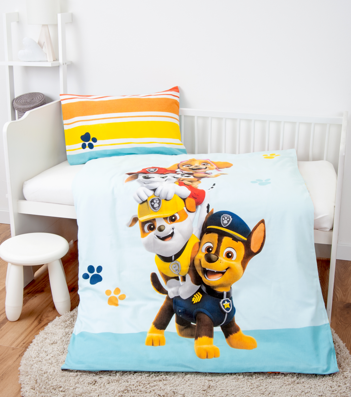 Renforcé-Bettwäsche mit buntem Paw Patrol-Motiv, bestehend aus einem Kissenbezug mit Streifenmuster und einer Bettdecke mit fröhlichen Hundemotiven, auf einem Kinderbett von schräg oben fotografiert.