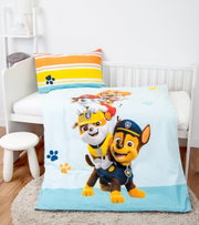 Renforcé-Bettwäsche mit buntem Paw Patrol-Motiv, bestehend aus einem Kissenbezug mit Streifenmuster und einer Bettdecke mit fröhlichen Hundemotiven, auf einem Kinderbett von schräg oben fotografiert.