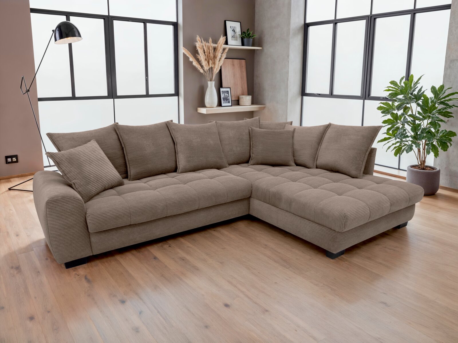 Modernes L-förmiges Ecksofa in Taupe mit Cordbezug, tiefer Sitzfläche und rechter Ottomane, frontal in leicht schräger Perspektive im hellen Wohnzimmer fotografiert.