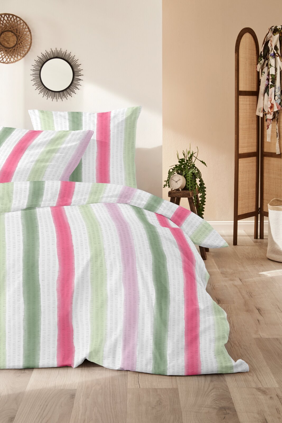 Gestreifte Bettwäsche in Weiß mit vertikalen Streifen in Grün, Pink und Flieder, auf einem gemachten Bett im Schlafzimmer – Frontansicht mit leichter Schrägperspektive von vorne.