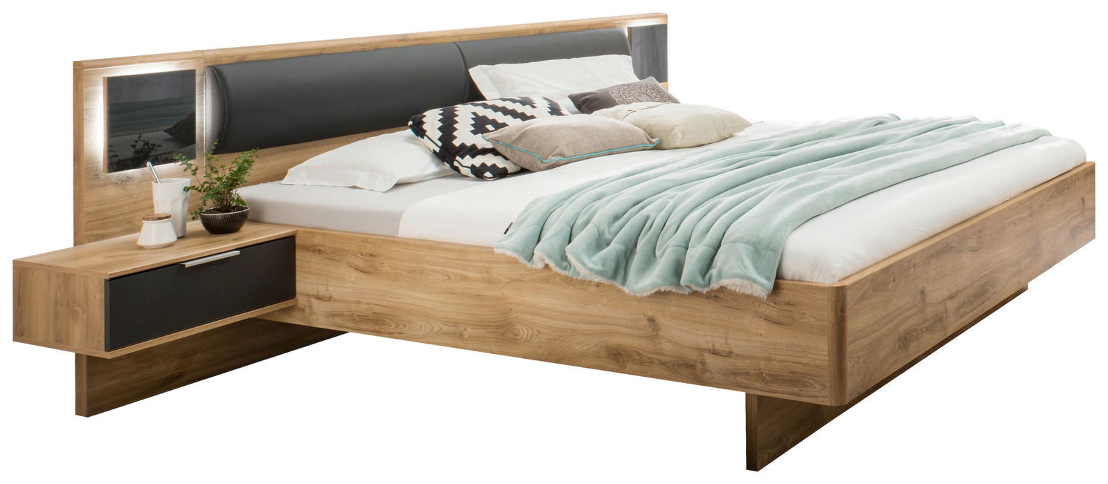Holzbett mit integriertem Nachttisch, Kopfteil mit schwarzem Polster und dekorativen Kissen, seitliche Perspektive