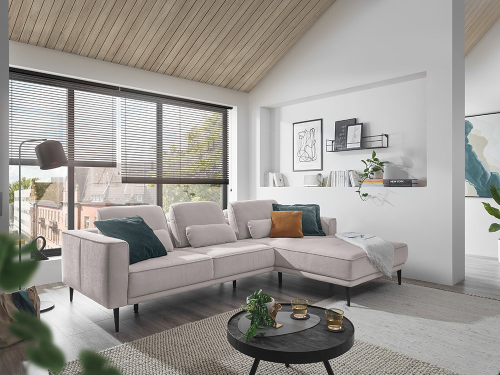 Ein helles Wohnzimmer mit einem beigen Ecksofa und einem schwarzen runden Couchtisch.