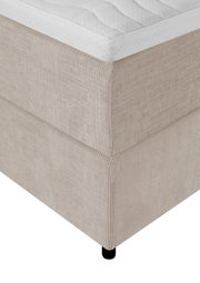 Detailaanzicht van bovenaf op de hoek van een beige boxspring met geribbelde stoffen bekleding, wit matras en zwart pootje