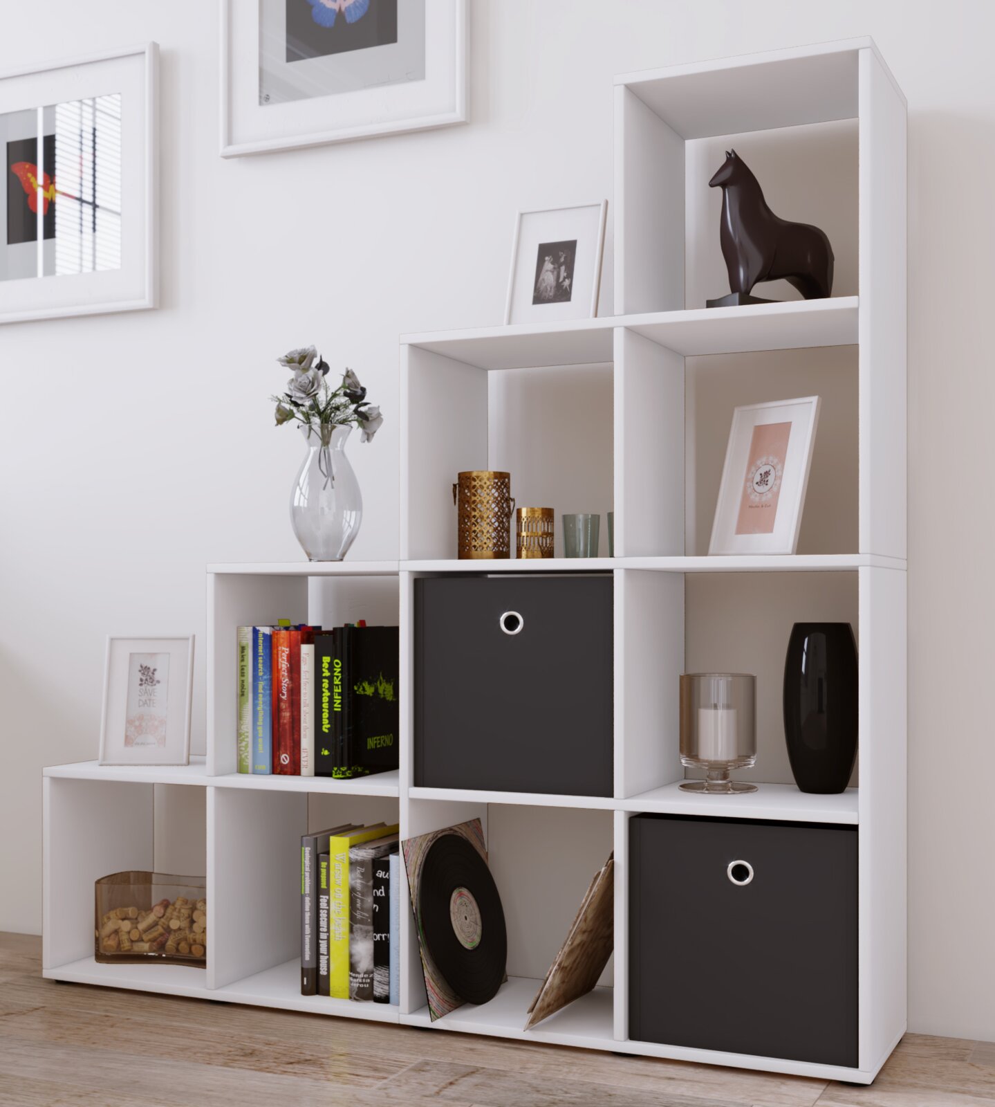 Modernes weißes Würfelregal mit mehreren Fächern, teils mit schwarzen Stoffboxen, dekoriert mit Büchern, Bildern, Vase und Kerzenhaltern; Perspektive: frontale Ansicht leicht von links.