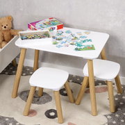 Kinderzimmer-Set aus weißem Kindertisch mit abgerundeten Ecken und zwei passenden Hockern mit Holzbeinen, auf dem Tisch liegen Puzzle-Teile und eine Puzzle-Schachtel; Ansicht schräg von vorne leicht von oben.