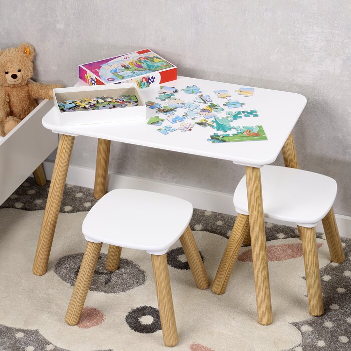Kinderzimmer-Set aus weißem Kindertisch mit abgerundeten Ecken und zwei passenden Hockern mit Holzbeinen, auf dem Tisch liegen Puzzle-Teile und eine Puzzle-Schachtel; Ansicht schräg von vorne leicht von oben.