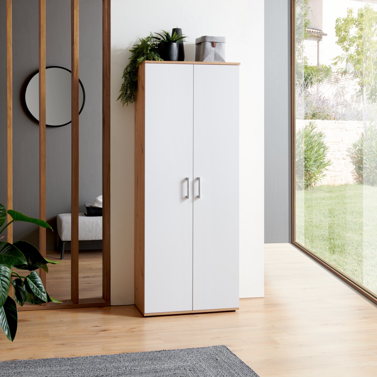 XORA XL-schoenenkast ALEX Moderne XL-schoenenkast in wit met houten frame, gefotografeerd vanaf de voorkant, in een lichte ruimte met planten en een groot raam.