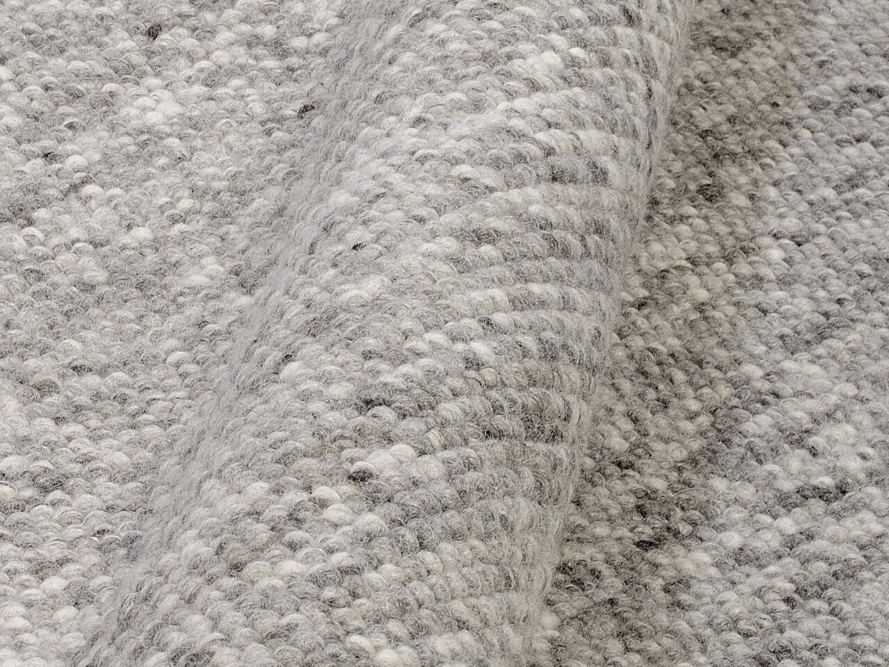 Nahaufnahme eines handgewebten Teppichs in Grautönen, der die Textur und das Muster des Materials zeigt.