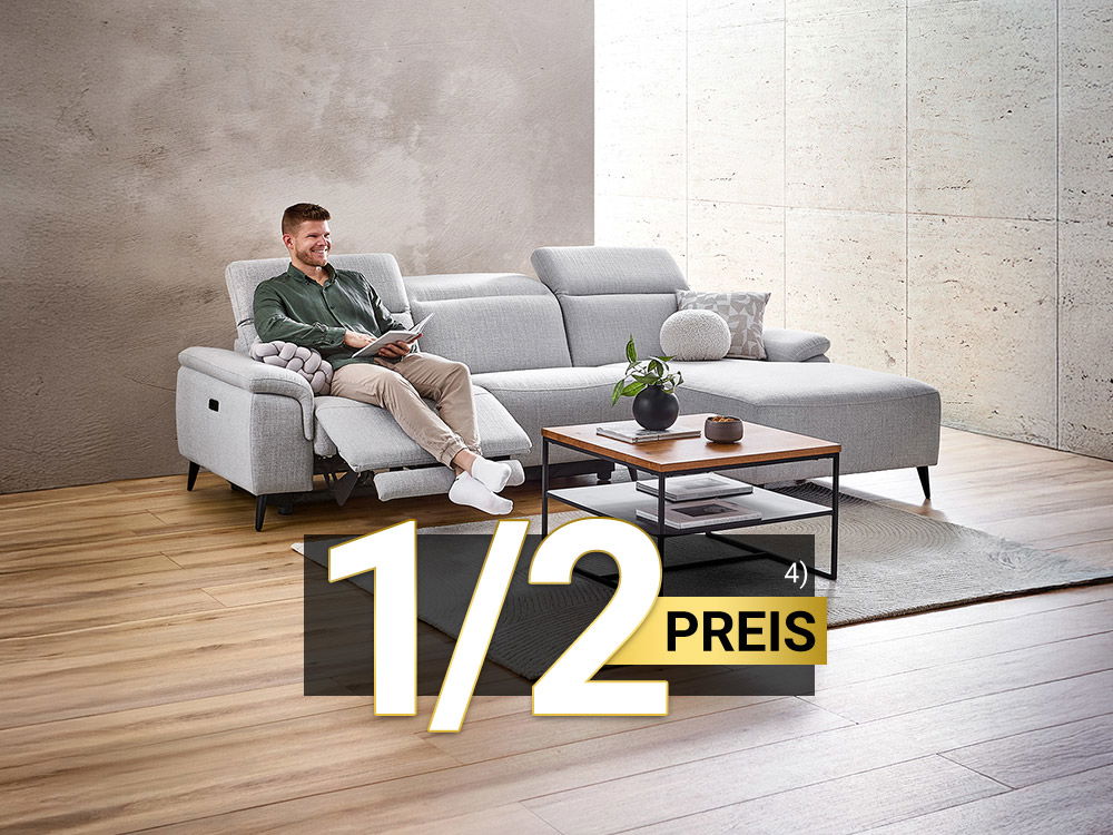 Mann entspannt auf grauem Ecksofa mit Relaxfunktion im modernen Wohnzimmer, Kaffeetisch davor, 1/2 Preis Hinweis