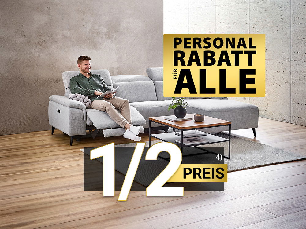 Mann entspannt auf grauem Ecksofa mit Relaxfunktion im modernen Wohnzimmer, Kaffeetisch davor, 1/2 Preis & Personal Rabatt für Alle Hinweis