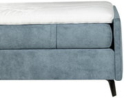 Nahaufnahme eines blauen Boxspringbetts mit weißem Topper, seitliche Perspektive
