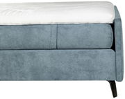 Nahaufnahme eines blauen Boxspringbetts mit weißem Topper, seitliche Perspektive