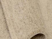 Nahaufnahme eines beigen Wollteppichs mit leicht melierter Struktur, von der Seite betrachtet.