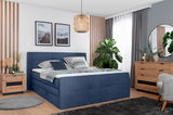 Modernes Boxspringbett in Blau mit Kissen und Decken, umgeben von stilvoller Dekoration in einem gemütlichen Schlafzimmer, seitliche Perspektive.