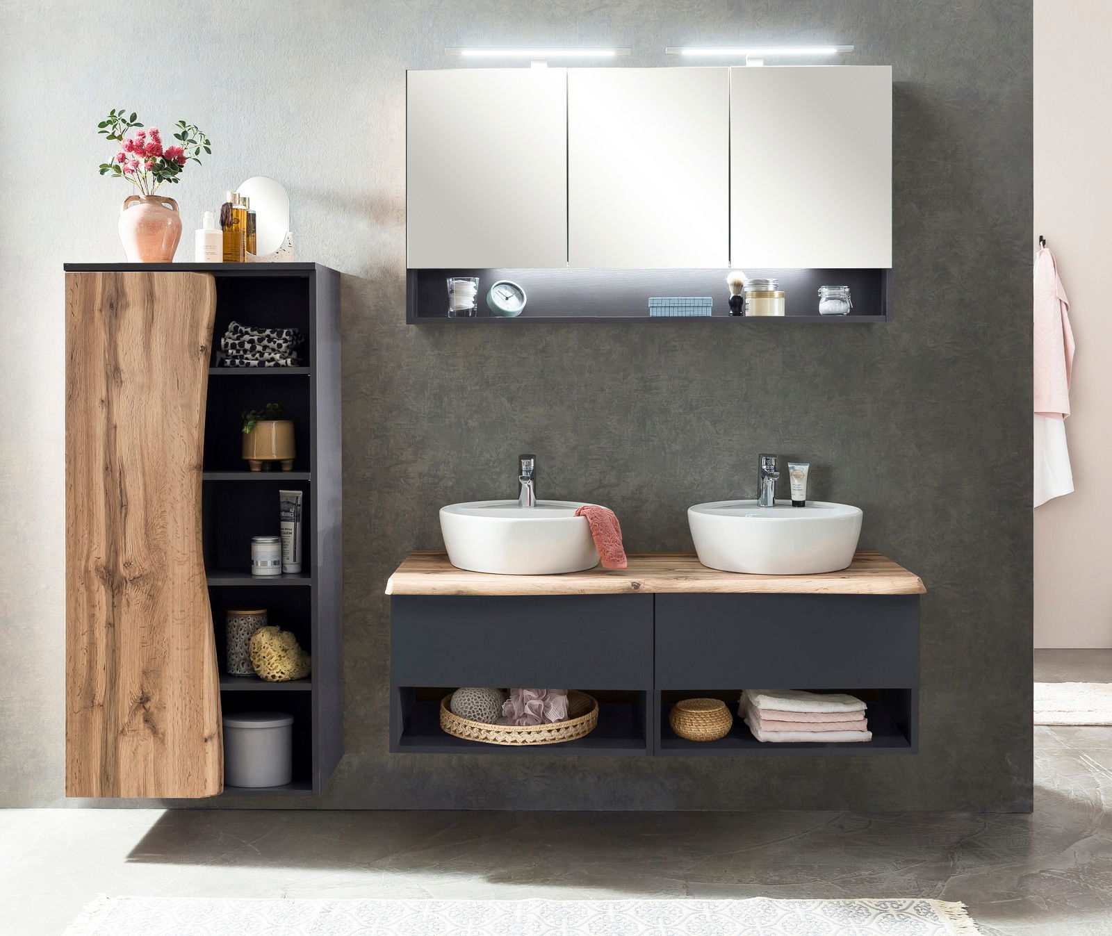 Modernes Waschtisch-Set mit zwei runden Waschbecken auf einer Holzplatte, darunter Stauraum mit Handtüchern und Körben, seitlich ein Schrank mit Holz- und dunklen Elementen, frontal betrachtet.