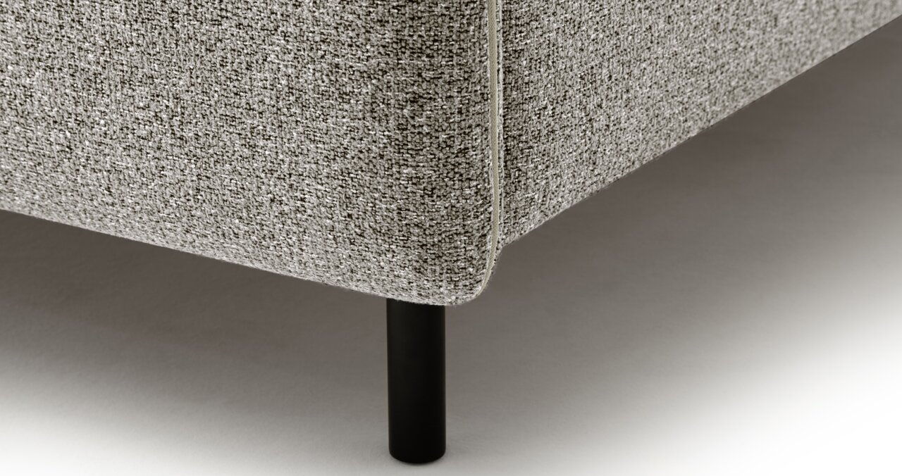 Close-up van een gestoffeerd bed met grijze bekleding en zwarte poten, gezien vanaf de zijkant