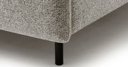 Close-up van een gestoffeerd bed met grijze bekleding en zwarte poten, gezien vanaf de zijkant