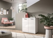 Weiße Kommode mit vier Schubladen, dekoriert mit Vasen und Büchern, in einem modernen Wohnzimmer mit Pflanzen und einem rosa Stuhl, seitliche Perspektive.