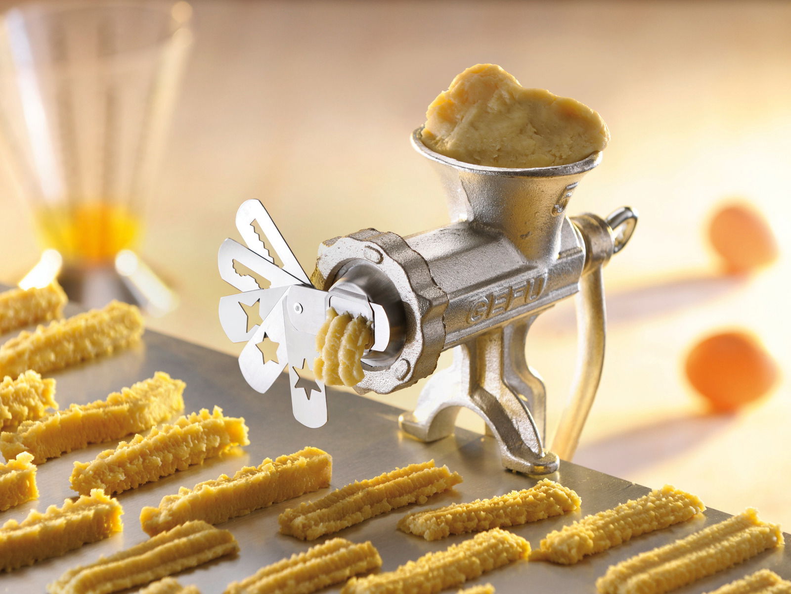 Nahaufnahme eines Spritzgebäckvorsatzes, der Teig in verschiedenen Formen auf ein Backblech presst.