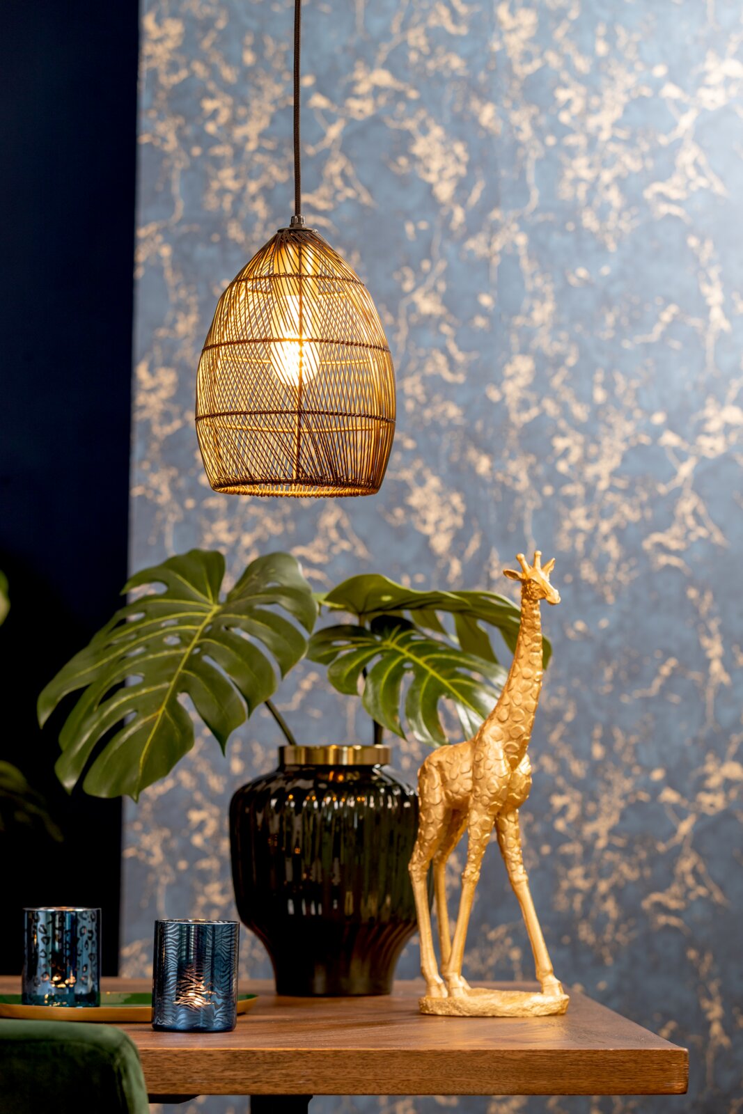 Frontaal aanzicht van een warm brandende hanglamp met een ovale, opengewerkte metalen kap boven een stijlvol houten dressoir.