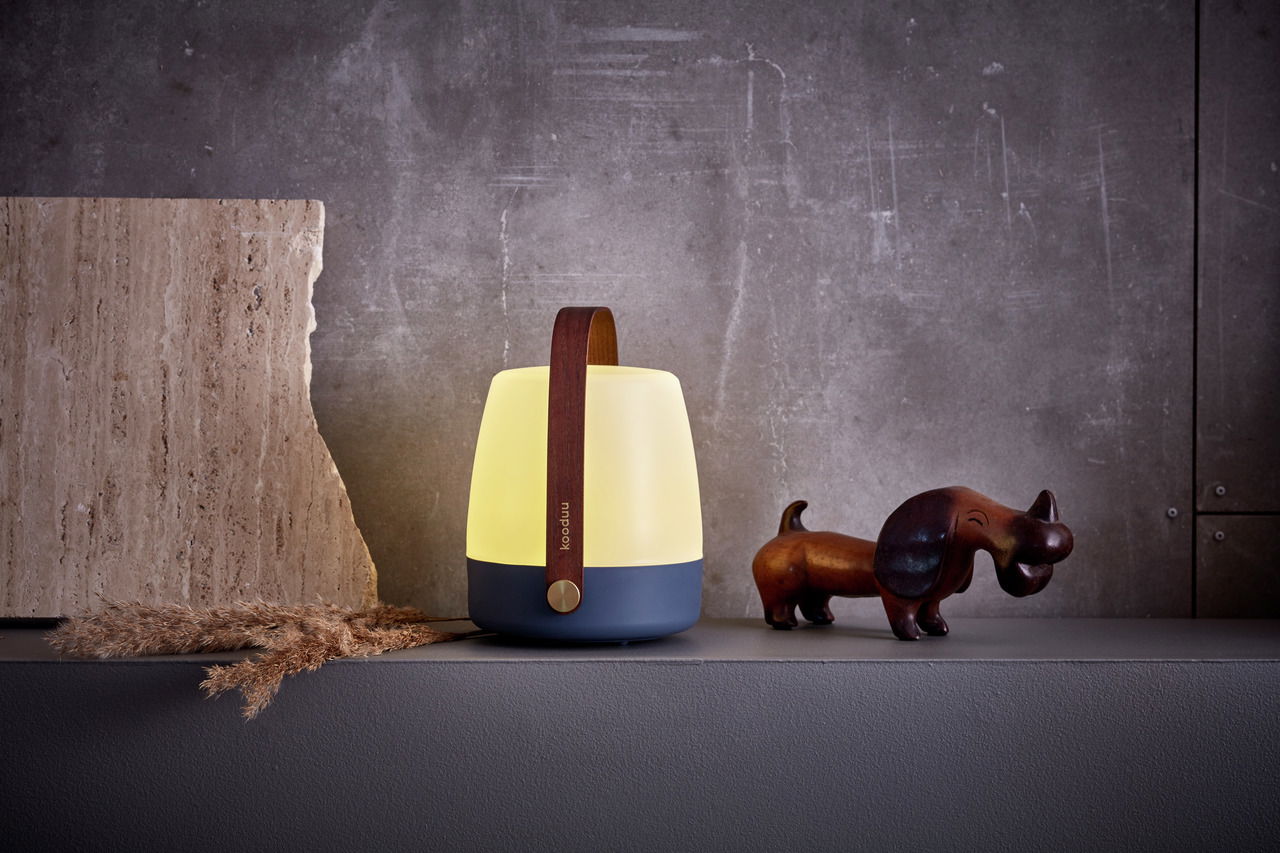 Stimmungsvolle Tischleuchte mit Holzgriff, seitliche Perspektive, neben einer Dekofigur und Naturmaterialien aufgestellt.