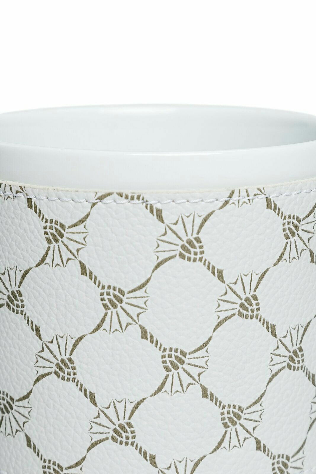 Nahaufnahme eines weißen Porzellanbechers mit grünem geometrischem Muster und genähter Textur.