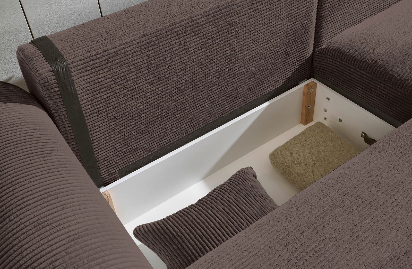 Nahaufnahme einer braunen Rundecke mit Stauraum, geöffnet, mit Kissen und Decke. Perspektive von oben.
