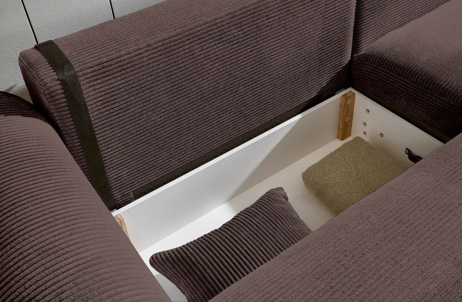 Nahaufnahme einer braunen Rundecke mit Stauraum, geöffnet, mit Kissen und Decke. Perspektive von oben.