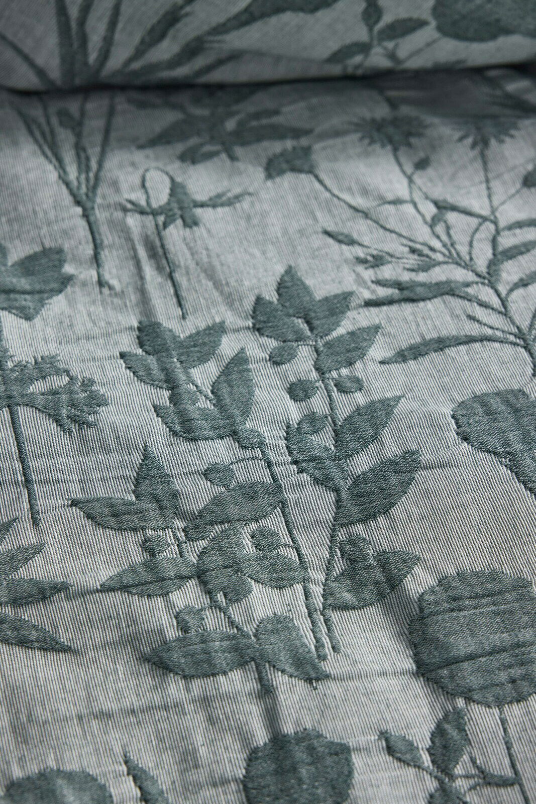 Nahaufnahme einer Bettwäsche mit floralem Muster in Grün auf grauem Hintergrund, von oben betrachtet.