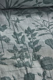 Nahaufnahme einer Bettwäsche mit floralem Muster in Grün auf grauem Hintergrund, von oben betrachtet.