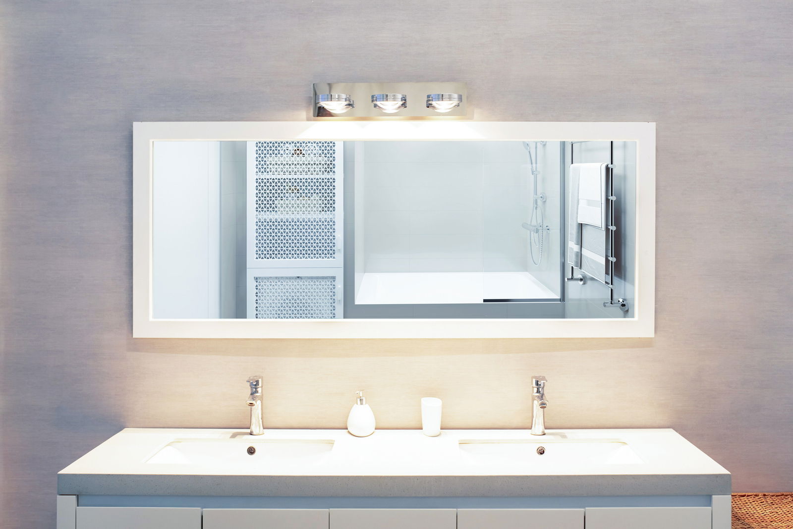 Moderne LED Wandleuchte über einem großen Spiegel in einem stilvollen Badezimmer, frontal betrachtet.