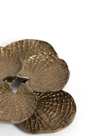 Nahaufnahme eines bronzefarbenen Wandornaments mit strukturierter, blattähnlicher Oberfläche, von oben betrachtet.