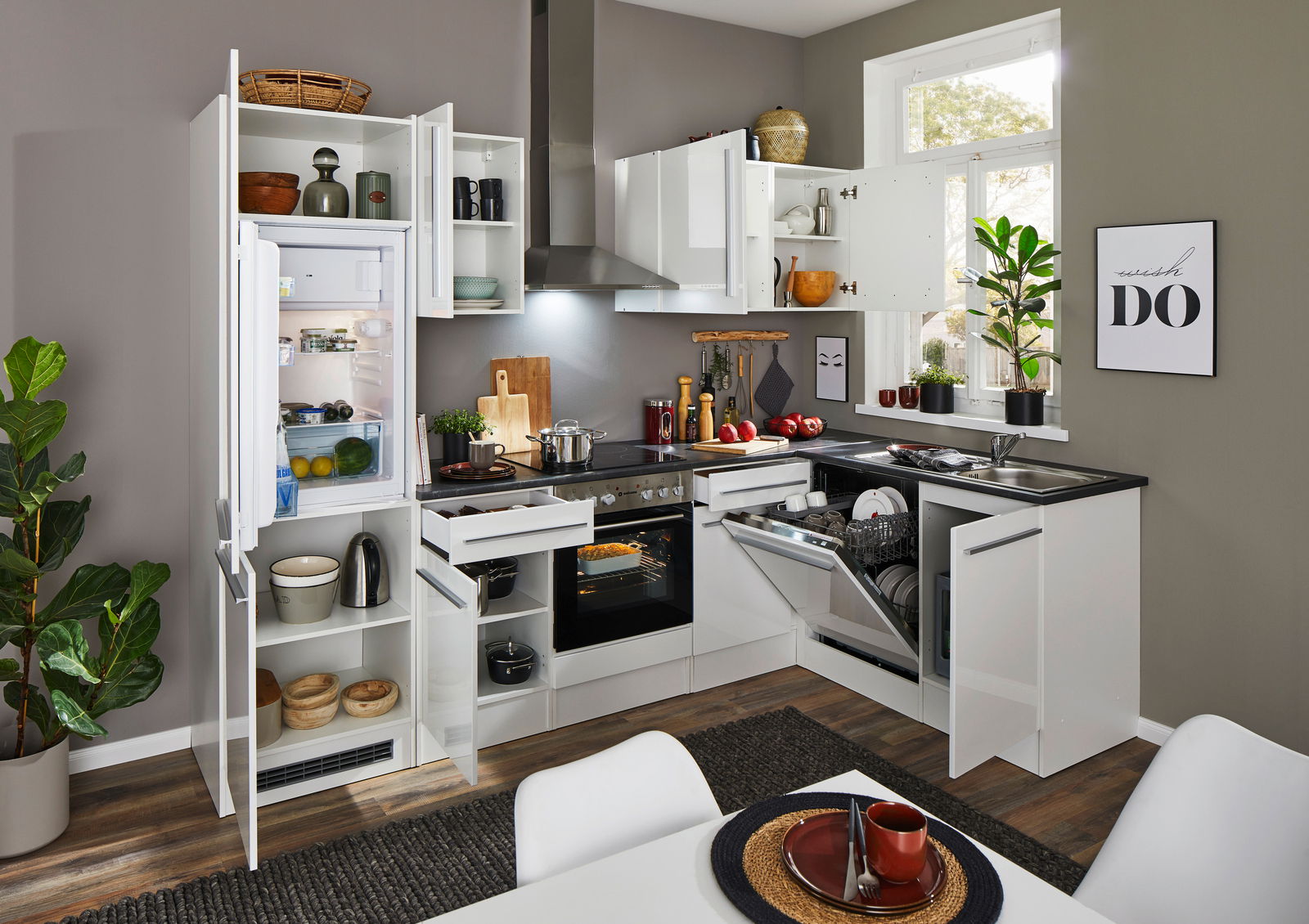 Moderne Küche mit Eckunterschrank, geöffnetem Kühlschrank, Geschirrspüler und Herd, aus der Perspektive eines Esstisches fotografiert.