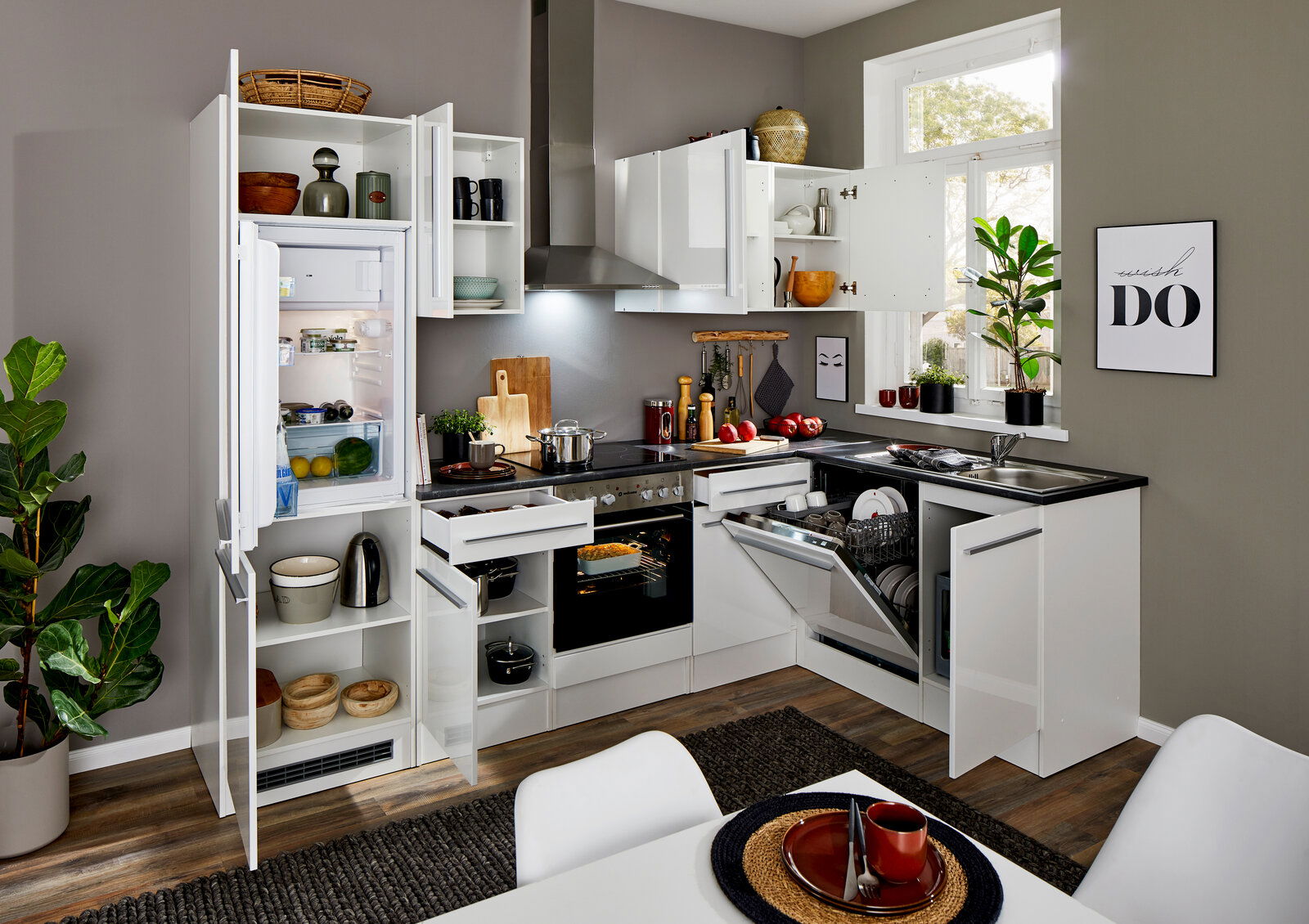 Moderne Küche mit Eckunterschrank, geöffnetem Kühlschrank, Geschirrspüler und Herd, aus der Perspektive eines Esstisches fotografiert.