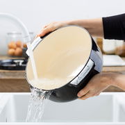 Gusseiserner Bräter rund 26cm in Schwarz, wird in der Küche unter fließendem Wasser gereinigt, seitliche Perspektive.