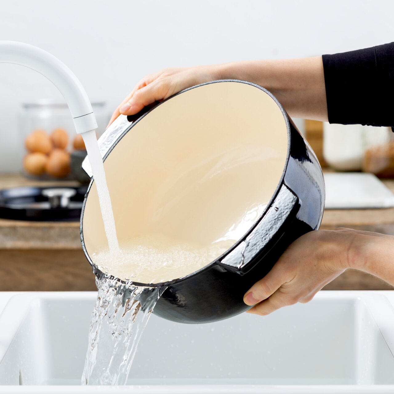 Ronde gietijzeren braadpan van 26 cm in zwart, wordt in de keuken onder stromend water schoongemaakt, zijaanzicht.