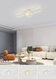 Moderne LED-Deckenleuchte in Weiß mit überlappenden, rechteckigen Lichtschlaufen, warmweiß leuchtend, montiert an der Wohnzimmerdecke; Ansicht leicht von unten in Raum-Perspektive.