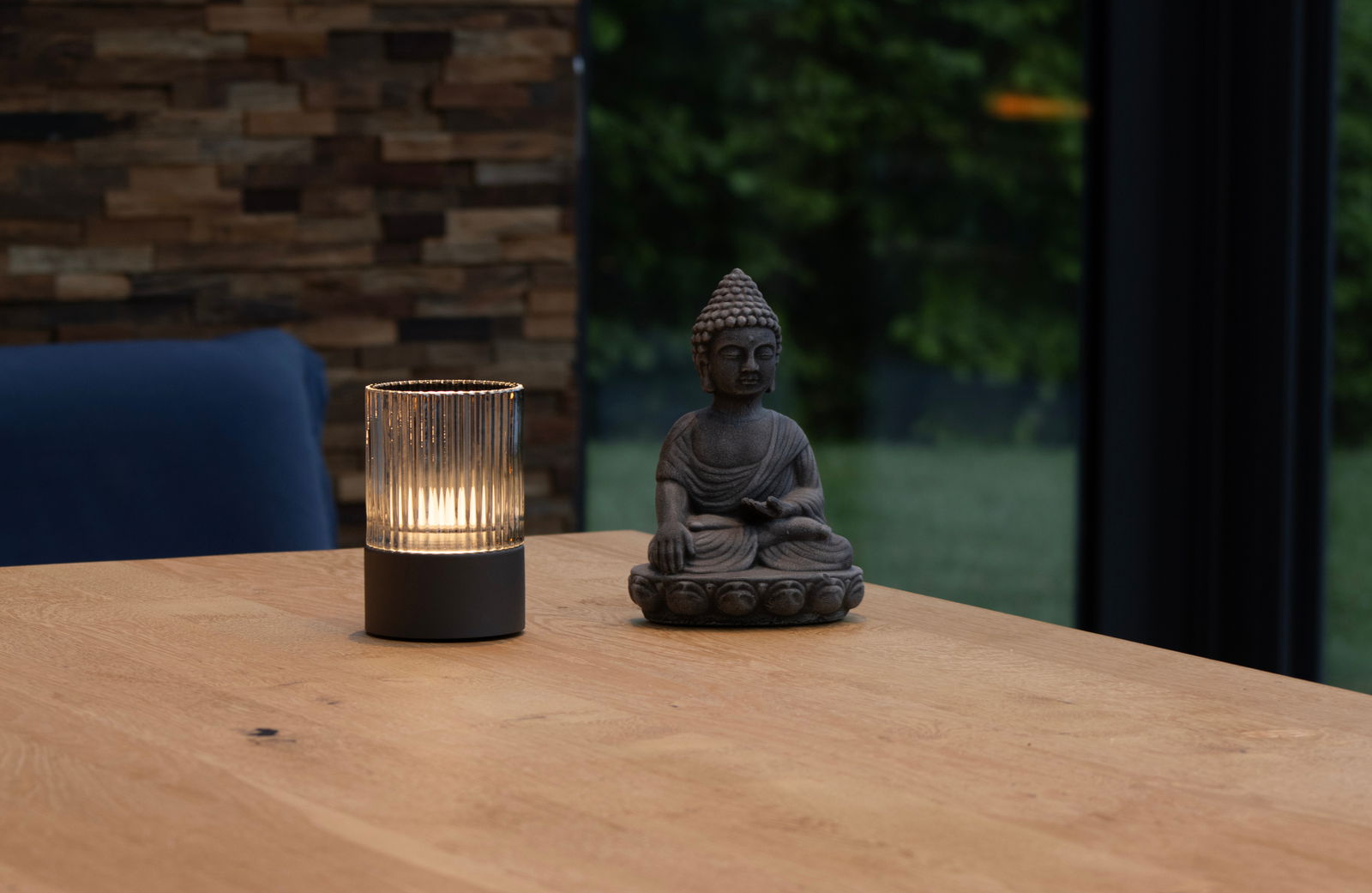 Fischer & Honsel ARIVA PRO windlicht op batterijen Akku-Windlicht auf einem Holztisch neben einer Buddha-Statue, seitliche Perspektive