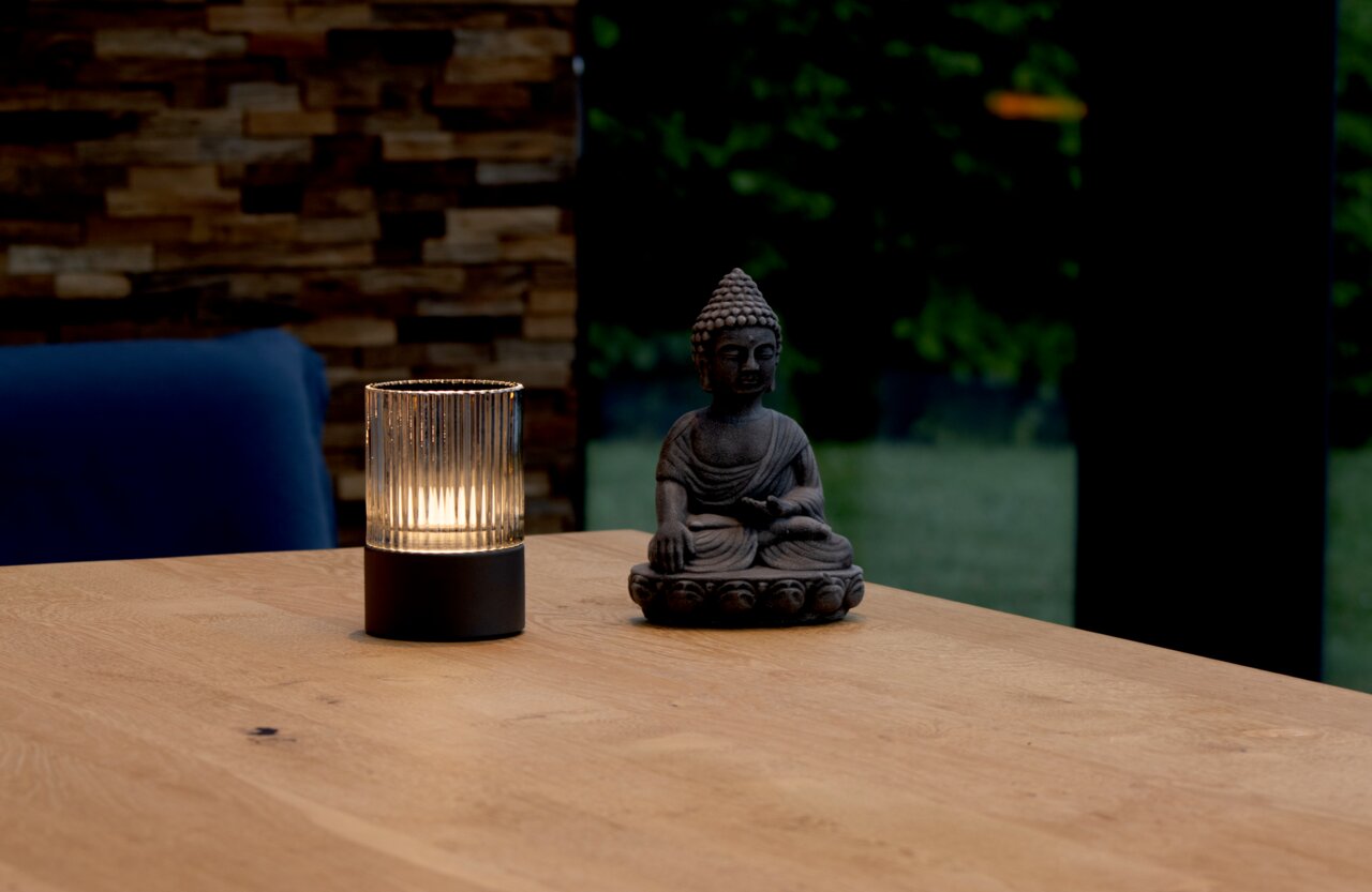 Akku-Windlicht auf einem Holztisch neben einer Buddha-Statue, seitliche Perspektive