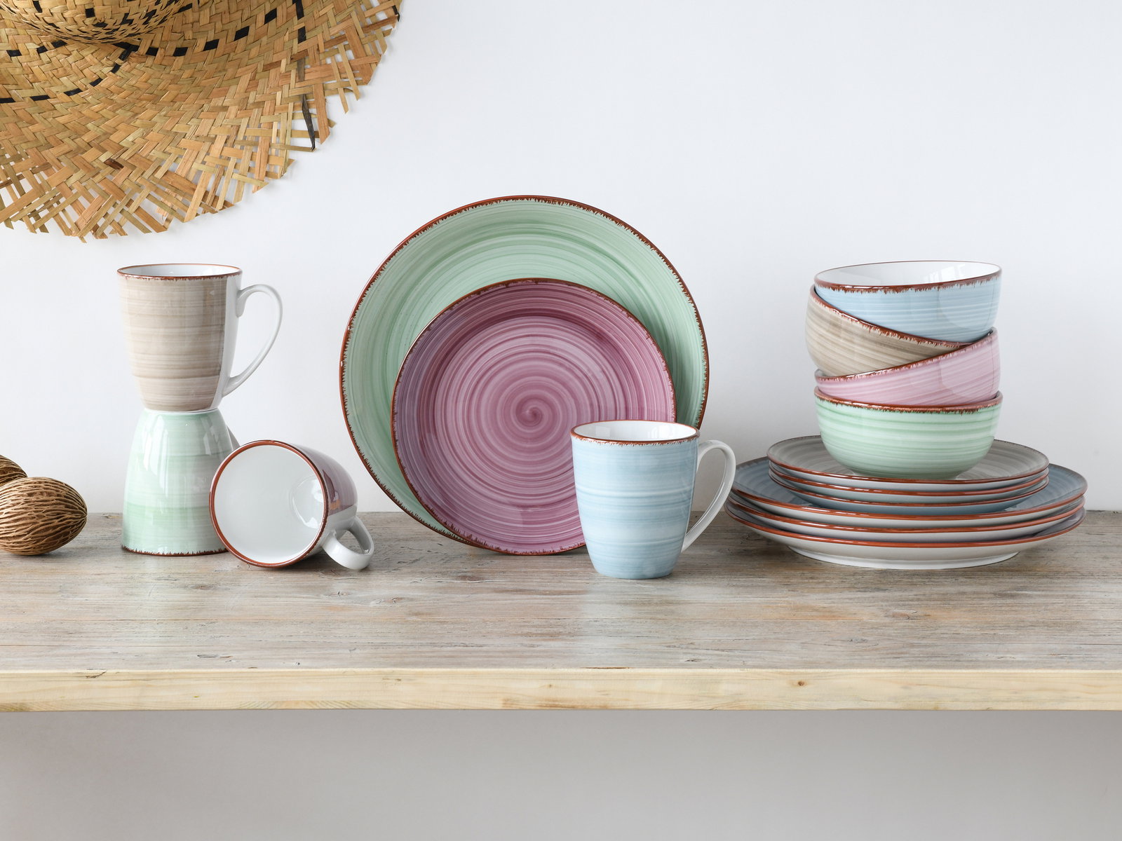Kombiservice 16-tlg in Pastellfarben, bestehend aus Tellern, Schalen und Tassen, auf einem Holztisch arrangiert. Frontalansicht.