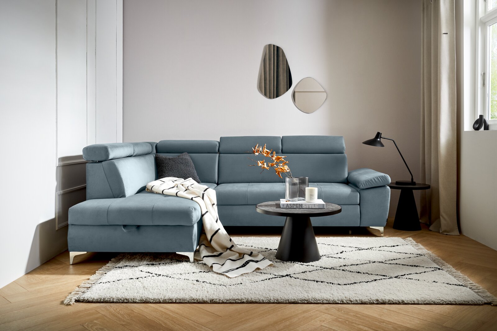 Moderne L-vormige hoekbank in een stijlvolle woonkamer, met blauwe bekleding, versierd met kussens en een deken, gezien vanuit het perspectief linksvoor.