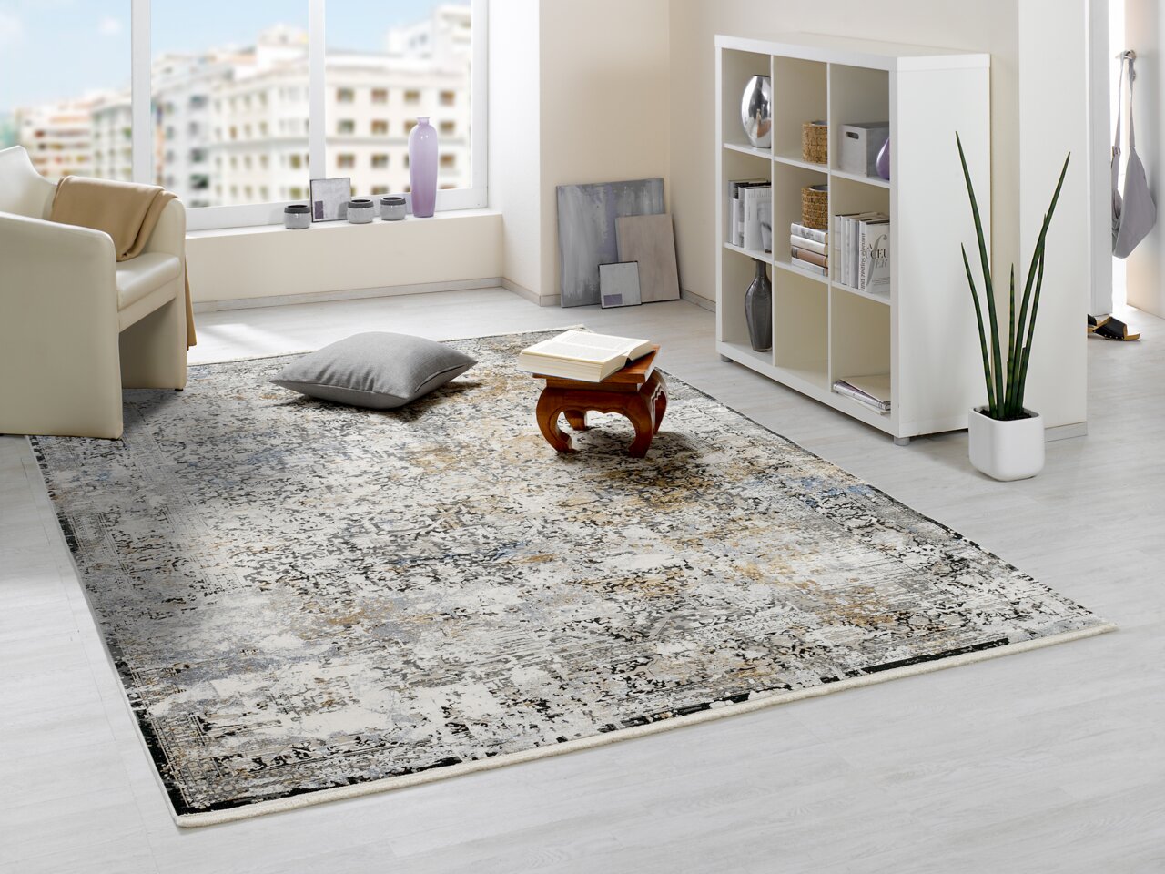 Designer Teppich in einem modernen Wohnzimmer mit hellem Boden, einem weißen Regal und einem Sessel. Perspektive von schräg oben.