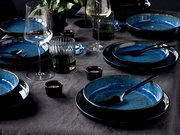 Elegantes 18-teiliges Tellerset in Blau, auf einem gedeckten Tisch mit Gläsern und Besteck, aus der Vogelperspektive fotografiert.